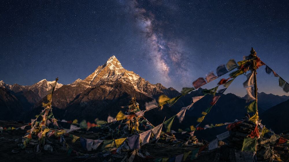 Prayer flags before a golden Himalayan peak under a starry sky